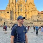 Peregrino que acabou de chegar à praça de obradoiro com a T-shirt da Comunidade do Caminho Português de Santiago e o Boné da Seta amarela.