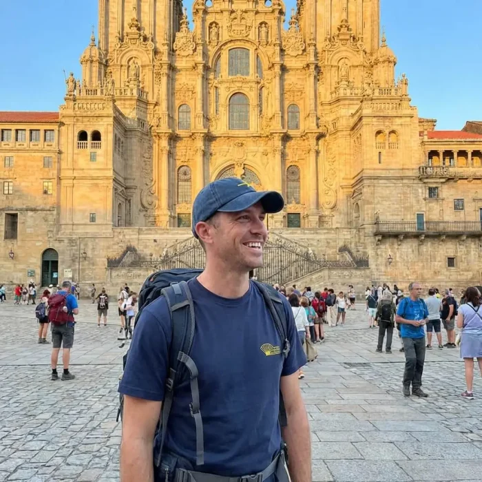 Peregrino que acabou de chegar à praça de obradoiro com a T-shirt da Comunidade do Caminho Português de Santiago e o Boné da Seta amarela.