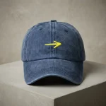 Boné da Seta Amarela em cor Denim, feito de algodão escovado, em cima de um pilar de cimento.