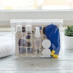 Plano aproximado do Necessaire Ultreya composto por duas embalagens de líquidos, duas caixinhas pequenas, uma venda para os olhos, os tampões para os ouvidos, e o postal checklist